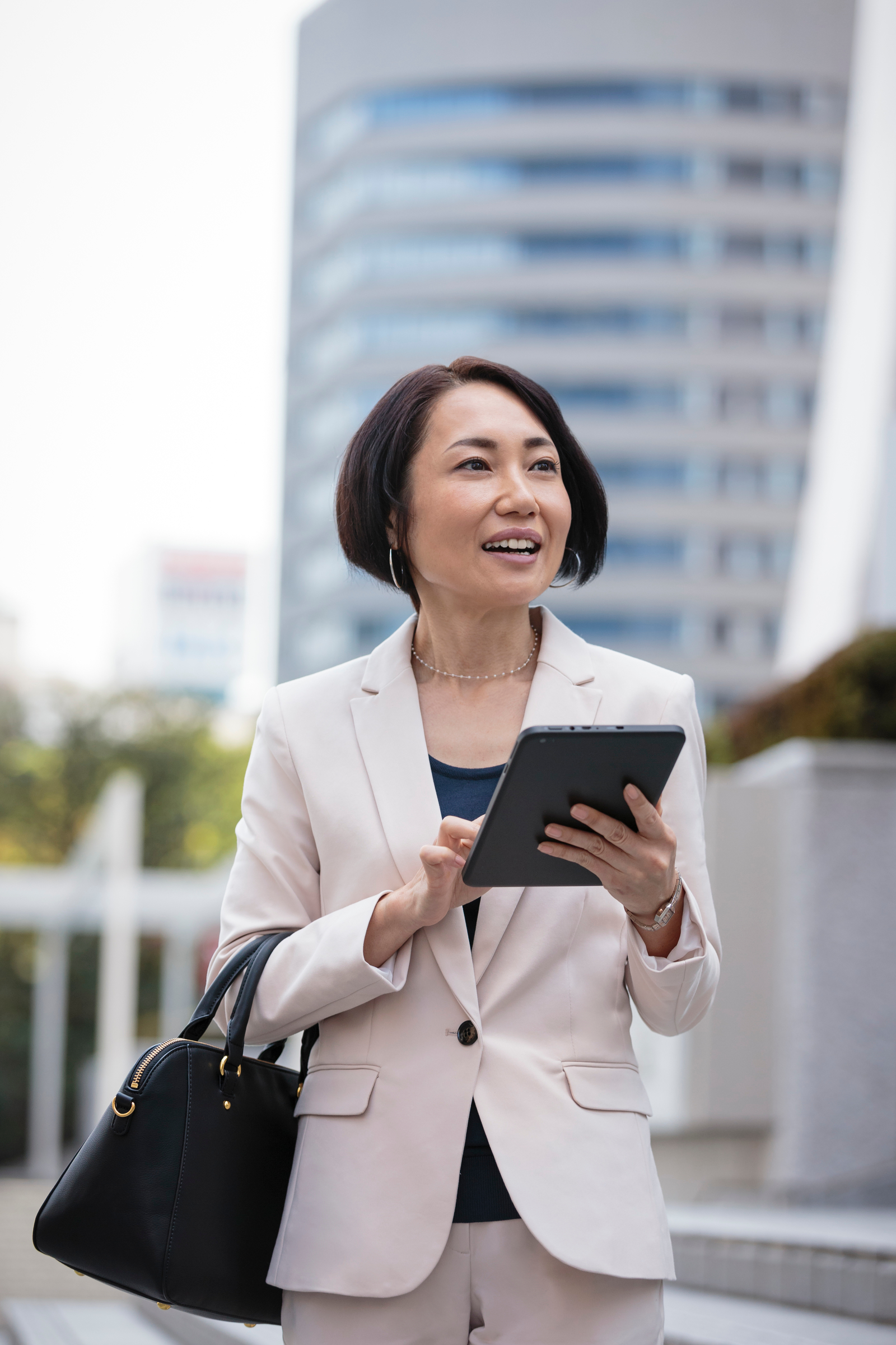 Close up of businesswoman using digital tablet and carrying briefcase walking under highrise buildings in cityscape Close up of businesswoman using digital tablet and carrying briefcase walking under highrise buildings in cityscape